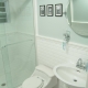 transitional guest hallway bathroom with white subway tile wainscot, light blue walls, pedestal ADA sink , tilt mirror, chrome fixtures, glass shower enclosure, and layered lighting plan