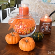 Living room wood slab table with DIY Halloween decor project. Glass vase wrapped in orange tulle ribbon holding candy corn next to tiny fresh pumpkins and squash with American Home by Yankee Candle fragrances