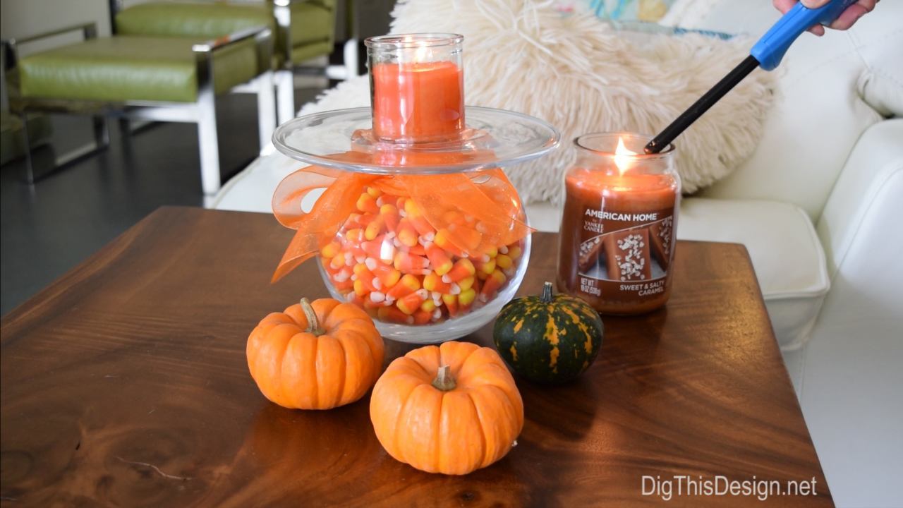 Living room wood slab table with DIY Halloween decor project. Glass vase wrapped in orange tulle ribbon holding candy corn next to tiny fresh pumpkins and squash with American Home by Yankee Candle fragrances