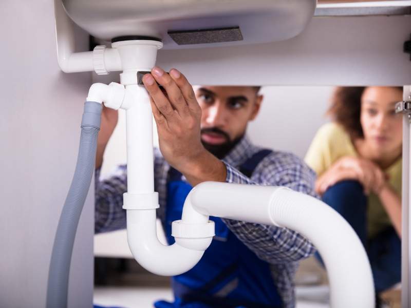 Plumber and home owner fixing pipes under bathroom sink