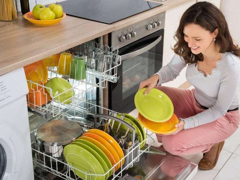 12 Common Dishwasher Problems and Their Solutions - lady in front of dishwasher with green and orange dishes.
