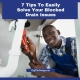 7 Tips To Easily Solve Your Blocked Drain Problems - plumber under sink with red wrench fixing the pipe.