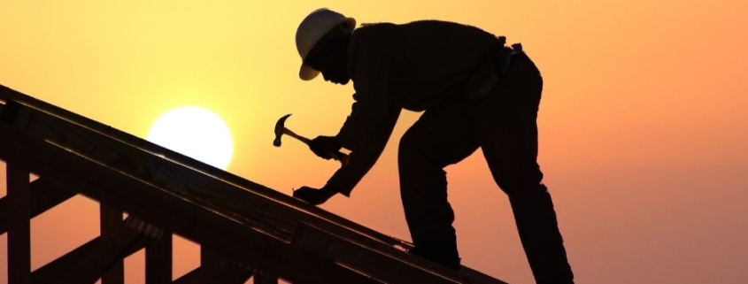 6 Reasons You Must Hire a Professional Roofer - shows man working on roof with sun setting in the background.