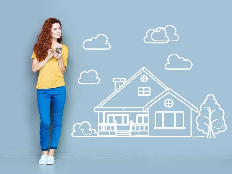 10 Important Facts to Know When Buying a House - Lady with long red hair, yellow top and blue jeans with white tennis shoes leaning on a light blue wall with a chalk drawing of a home.