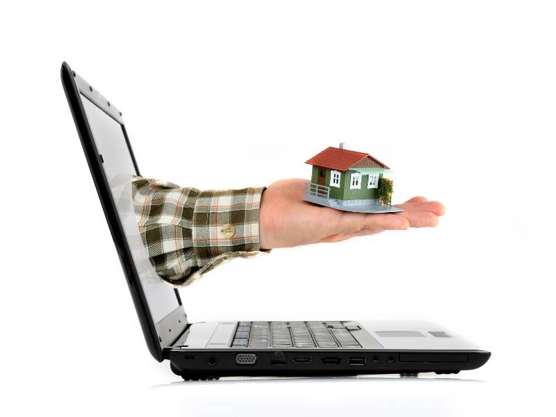 Looking Online to Buy Properties Consider These 5 Tactics! Laptop with mans hand holding a model home reaching out from the screen.